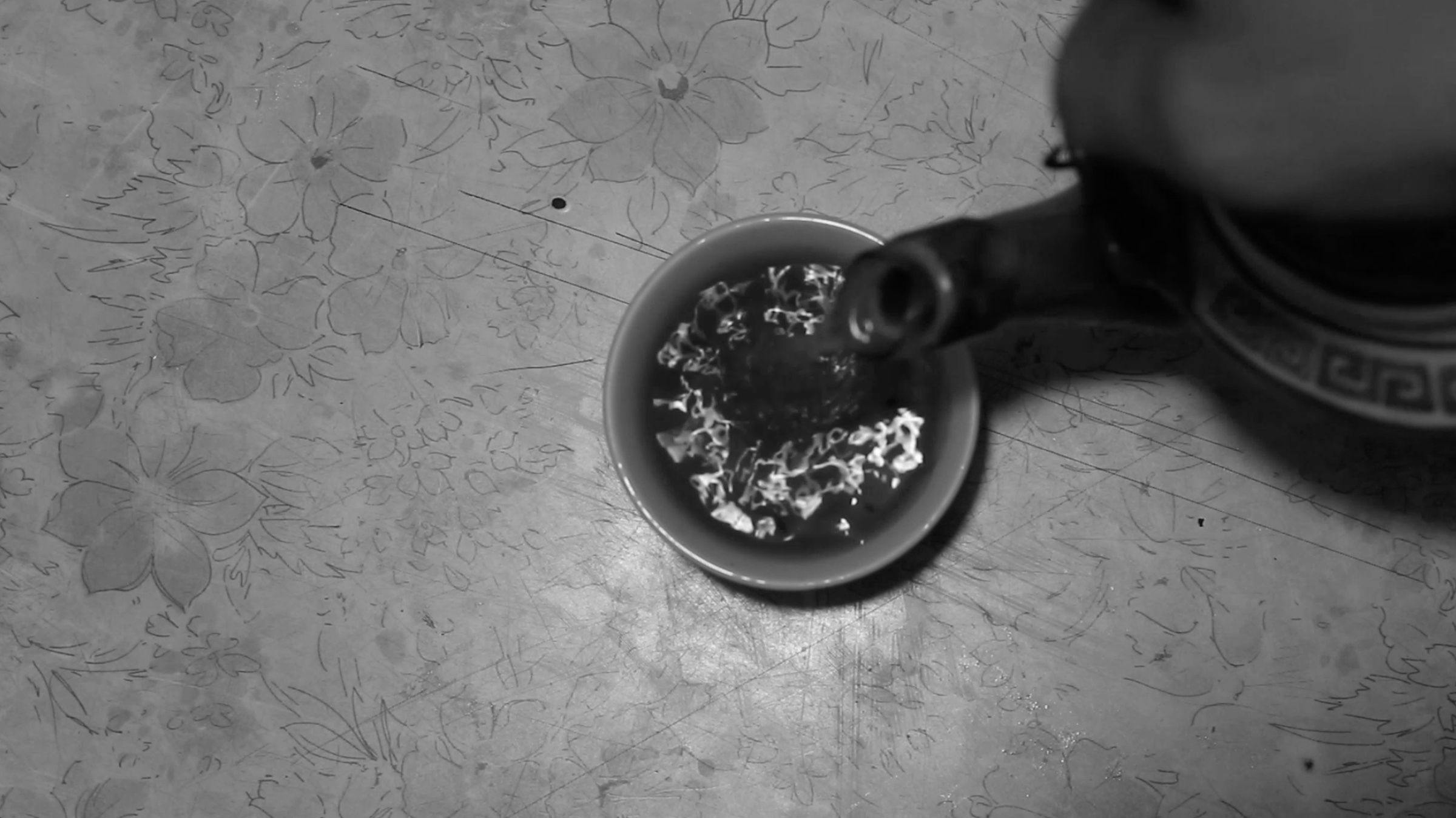 a black and white image of tea being poured into a cup