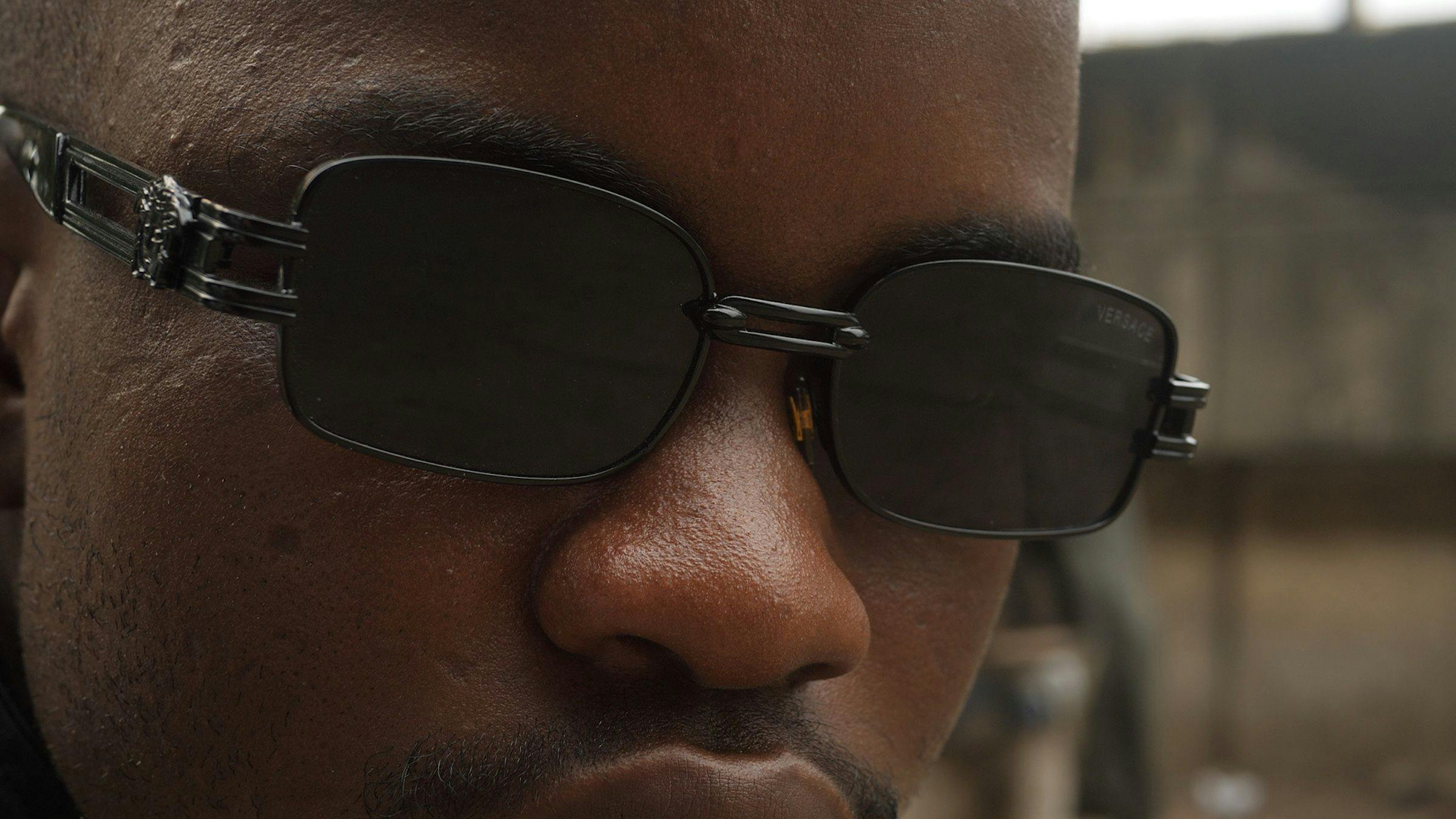 A close up of a black person's face. They are wearing sunglasses. 