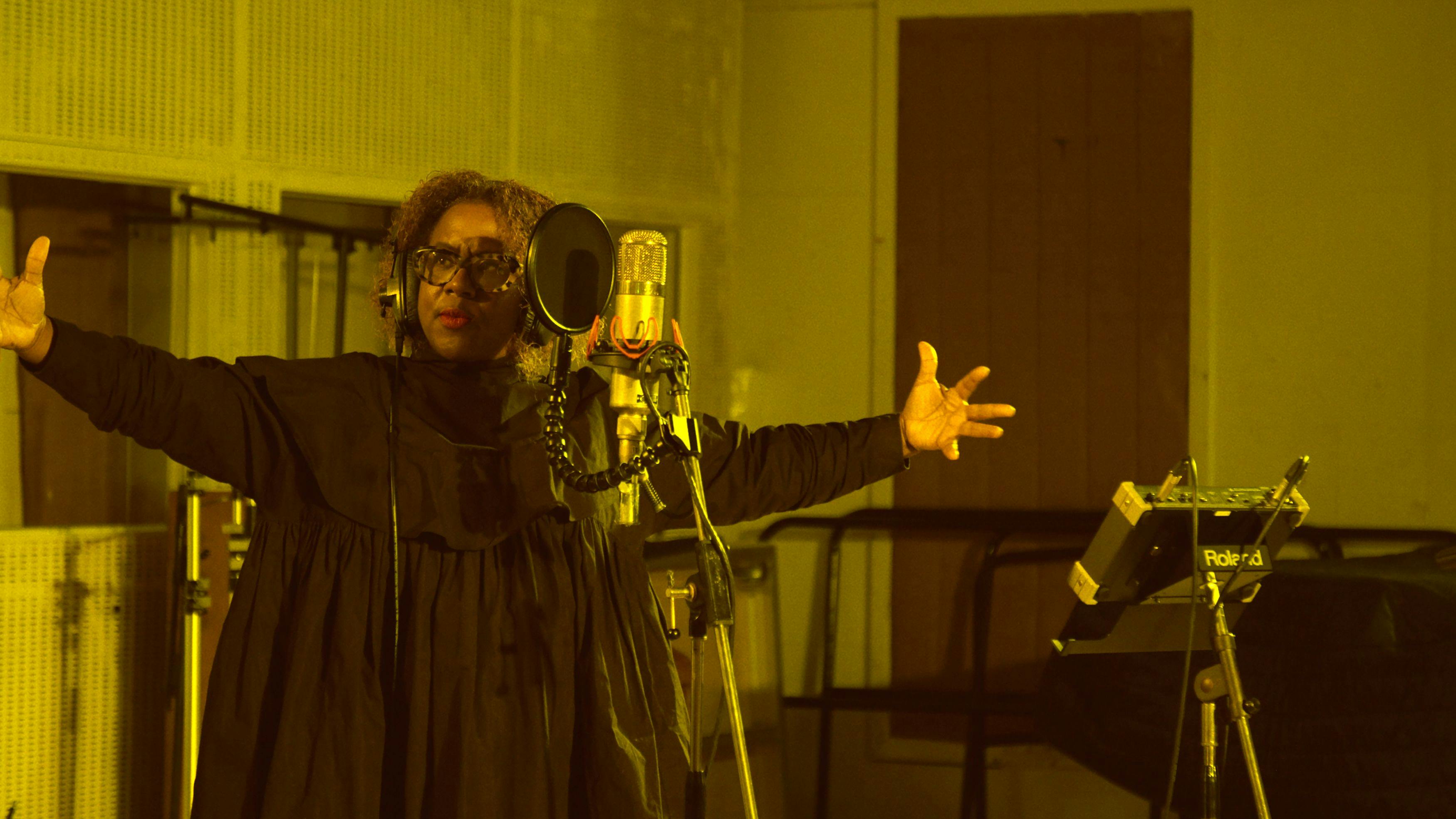 a black woman wearing a black dress is singing into a microphone in a recording studio