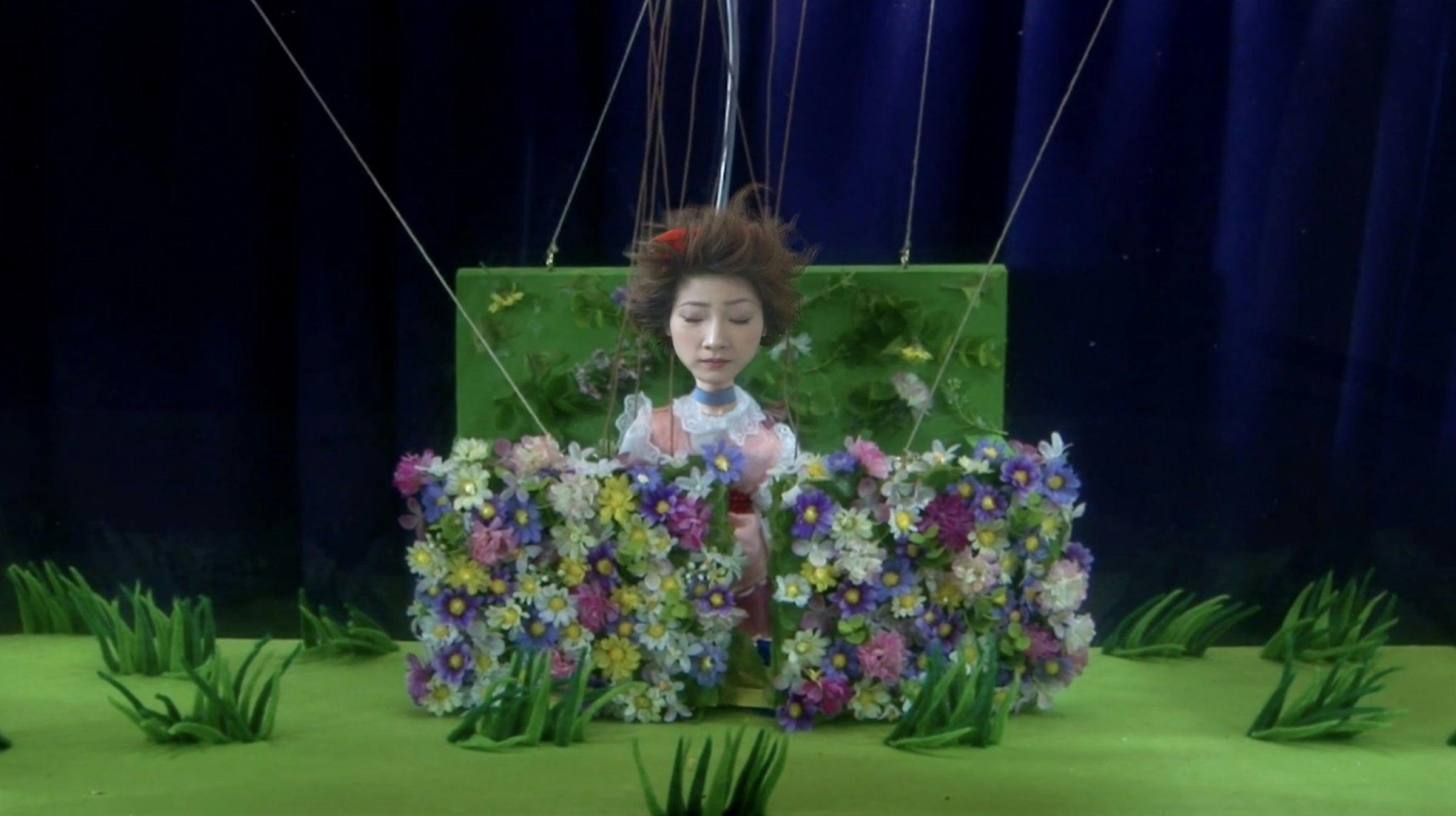 an image of a puppet whose strings are visible in a staged garden setting